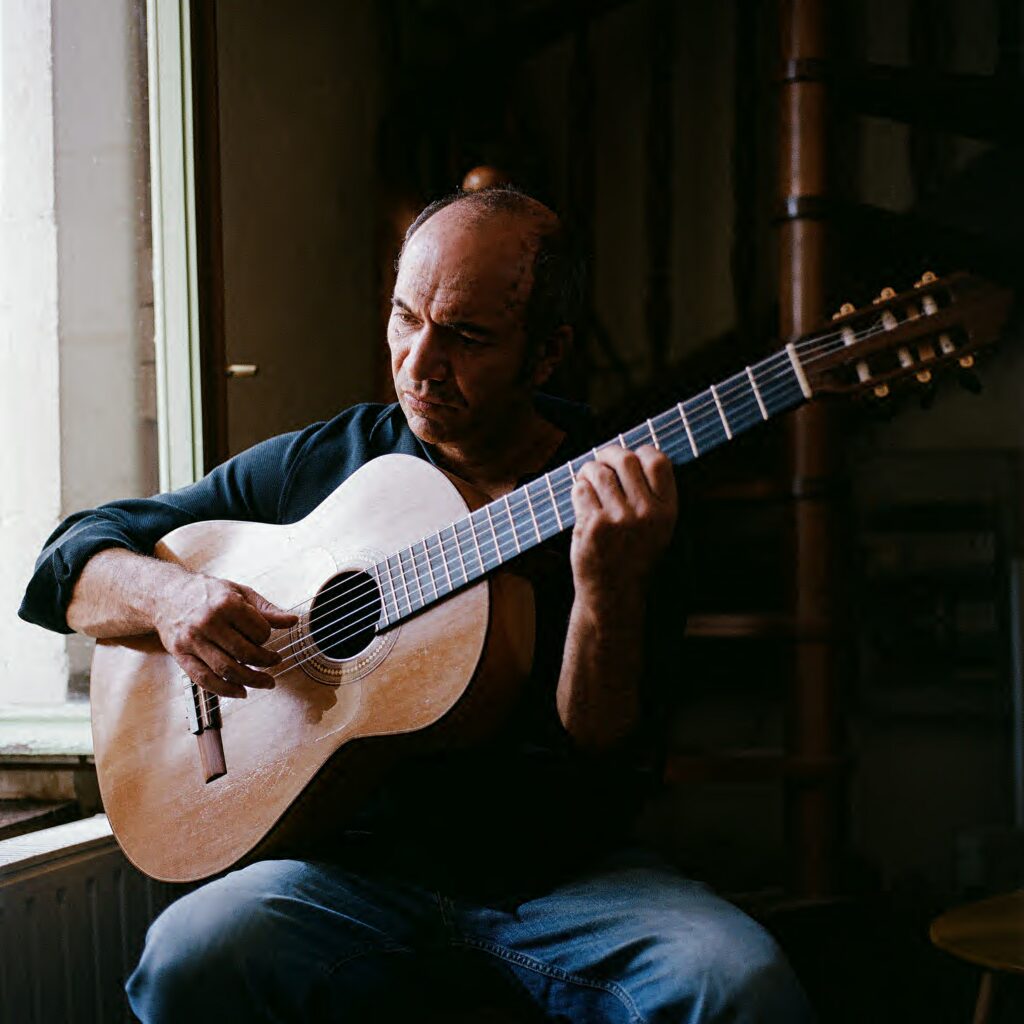 David Michelet playing classical guitar beside a window.